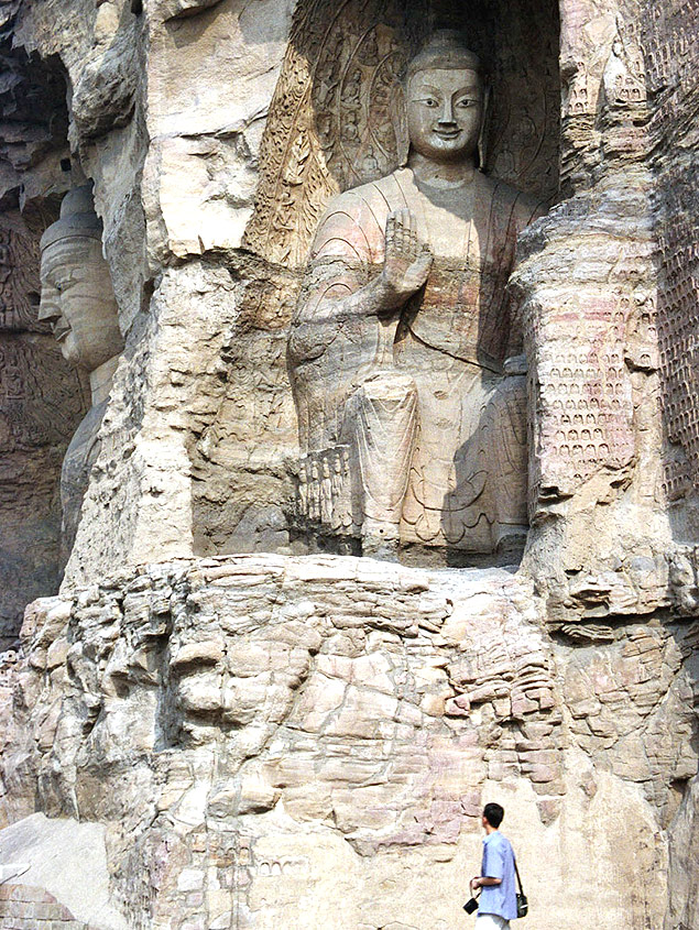 ORG XMIT: 464101_1.tif Turista passa ao lado de esttua de Buda em uma das cavernas de Yungang Shiku, em Datong, China. A maioria das esttuas do local foram escavadas na poca da dinastia Wei entre 460 e 494 D.C. O Budismo foi introduzido na China h 2 mil anos, unindo-se ao Confucionismo e ao Taoismo. (A tourist walks past a giant Buddha statue sitting in one of the more 20 caves of Yungang Shiku (Cloud Ridge), in Datong, China's Shanxi province, August 27, 2002. Most of the caves of the Yungang Shiku were carved during the Northern Wei dynasty, between AD 460 and 494. Buddhism has integrated with Chinese culture over the last 2,000 years, combining with Confucianism and Taoism in the process. Picture taken August 27. REUTERS/China Photo 