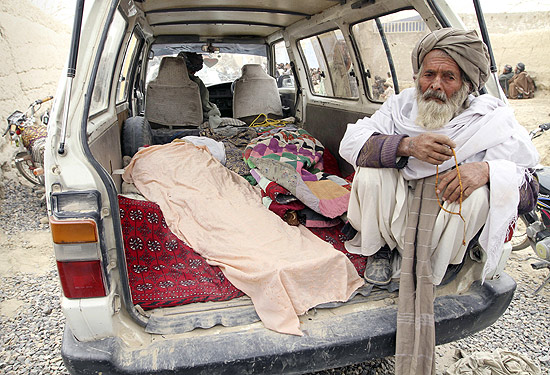 Afegão senta ao lado de corpos de vítimas de ataque de soldado americano em Candahar