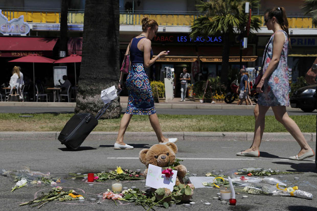 A woman pulls her suitcase as she walks past flowers and a stuffed toy placed in tribute to victims of the truck attack along the Promenade des Anglais on Bastille Day that killed scores and injured as many in Nice, France, July 17, 2016. REUTERS/Pascal Rossignol ORG XMIT: PAR242