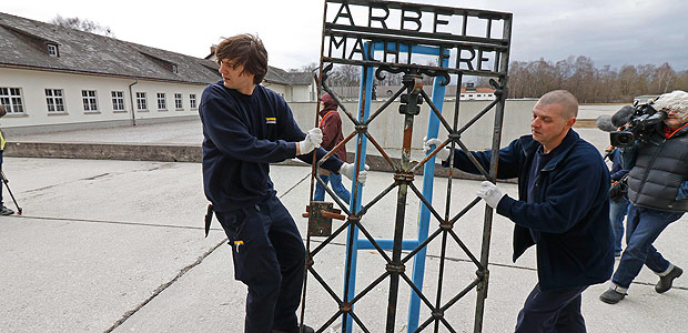 Two men move the original iron gate with the slogan "Arbeit macht frei" (work will set you free) over the grounds of the former Nazi concentration camp in Dachau, southern Germany, on February 22, 2017. The gate was brought back to the Dachau memorial site after it was stolen from the former Nazi concentration camp two years ago and was found in Norway at the end of the year 2016. / AFP PHOTO / UWE LEIN