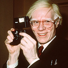 Warhol sorri com uma câmera fotográfica polaroid em foto tirada em 1976, em NY