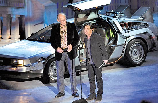 Os atores Christopher Lloyd (à esq.) e Michael J. Fox diante do carro futurista da cinessérie "De Volta para o Futuro"