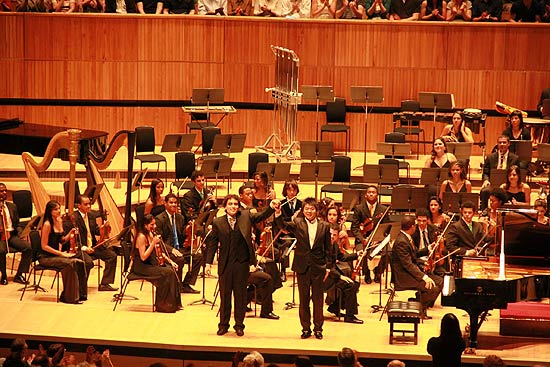 O maestro Ilyich Rivas ( esq.) e o pianista Lang Lang agredecem os aplausos no palco do Royal Albert Hall, em Londres, com a Orquestra Juvenil da Bahia (fundo)