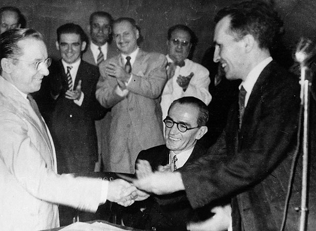 Sob o olhar de Graciliano Ramos (sentado), Luís Carlos Prestes (dir.) entrega a Cândido Portinari ficha de filiação ao PCB, nos anos 1940
