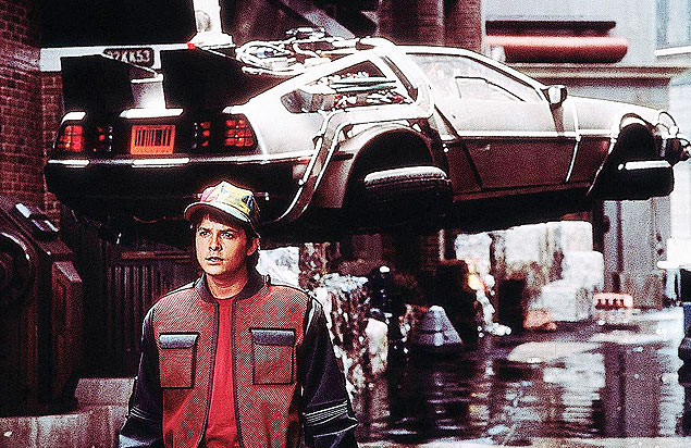 O ator Michael J. Fox com um modelo estilizado do carro De Lorean em cena de 'De Volta Para o Futuro'