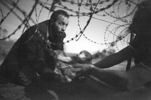Imagem do fotgrafo Warren Richardson, feita em Roszke, na Hungria, mostra refugiado passando beb por baixo de arame-farpado na fronteira hgaro-srvia