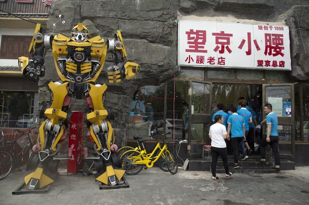 Workers prepare for business near a sculpture of a character from the Transformer movie used as a mascot in Beijing, China, Wednesday, July 5, 2017. Despite a quota on western movies in China, many identify with some of the popular characters from major blockbusters. (AP Photo/Ng Han Guan) ORG XMIT: XHG108 