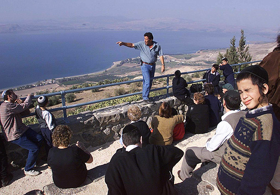 Turistas escutam guia do kibutz Kfar Haruv, em antiga base militar sria com vista para o mar da Galileia, em Gol