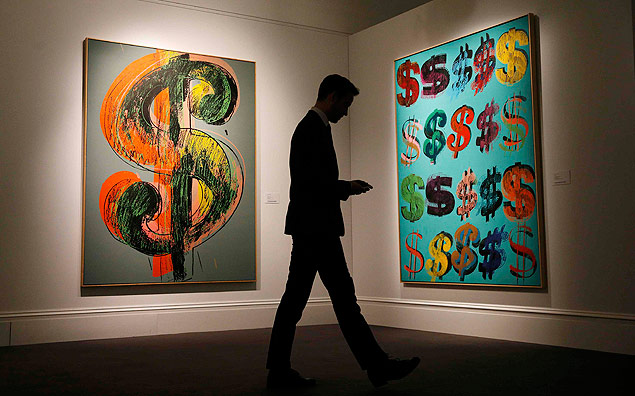 Homem diante das telas "Dollar Sign" e "Dollar Signs" (1981) na Sotheby's de Londres; em leilo dia 1/7, elas foram vendidas por cerca de R$ 23 milhes e R$ 34 milhes, respectivamente