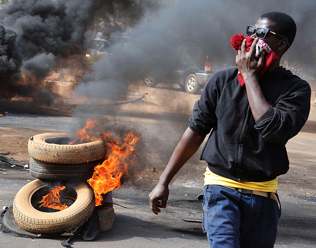 A man holds a hat over his mouth as black smoke billows from tyres set on fire in Niamey 