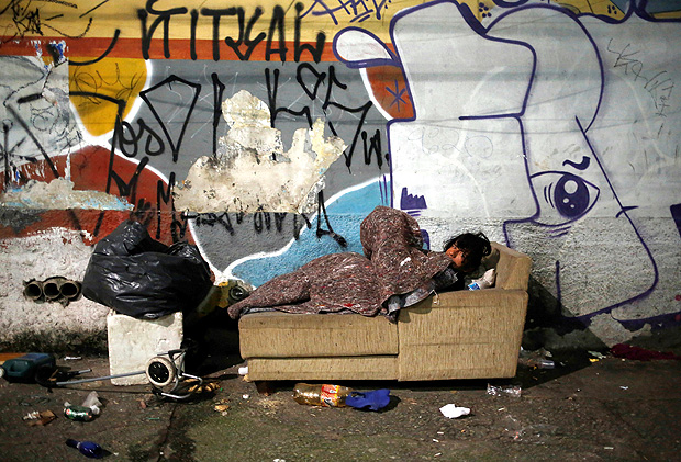 A homeless person covered in a blanket rests on a sofa on the street, on a cold night in Sao Paulo, Brazil