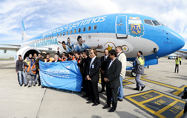 Aerolineas Argentinas' workers poses next to the airplane dacorated with the portraits of Argentina's National team footballers forward Lionel Messi (C), forward Gonzalo Higuain and forward Serio Aguero (L) that will transport Argentina's national football team to Brazil and back home at the end of the 2014 FIFA World Cup Brazil, during its presentation in Ezeiza, Buenos Aires on June 3, 2014. AFP PHOTO/Juan Mabromata ORG XMIT: MAB893