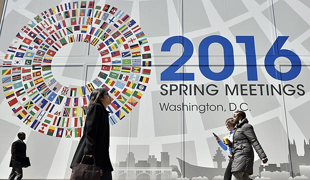 Pedestrians pass by a banner announcing the 2016 spring meetings of the International Monetary Fund (IMF) and World Bank outside of the IMF headquarters on April 6, 2016 in Washington, DC. The annual meeting runs from April 15-16. / AFP PHOTO / Mandel Ngan ORG XMIT: MNN017