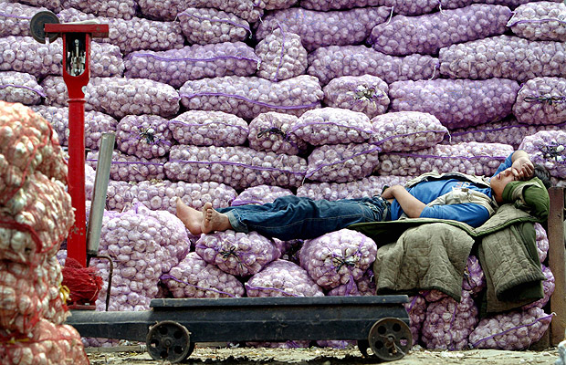 ORG XMIT: 450701_1.tif Vendedor de alho dorme em meio a sacas do produto em mercado de Pequim; o banco central da China disse que as medidas para desaquecer a economia j comeam a dar resultados. A Chinese garlic vendor sleeps on his produce as he waits for customers, at an outdoor market in Beijing, June 17, 2004. China's measures to cool its fast-growing economy have started showing results, Central Bank Chief Zhou Xiaochuan said on Thursday, sounding the latest official vote of confidence in current policies. REUTERS/Guang Niu 