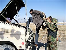 Soldado iraquiano ajuda suspeito preso a entrar na traseira de veculo em Bagd 