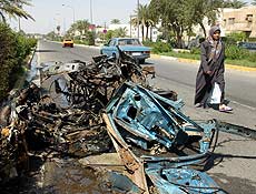 Mulher passa ao lado de carro destrudo em ataque suicida que matou 2 em Bagd