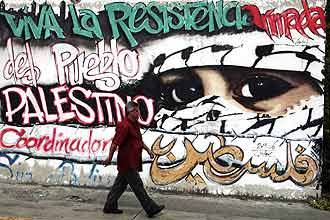 Homem caminha nas ruas de Caracas, na Venezuela, em frente a um grafite em repdio a ofensiva israelense na faixa de Gaza