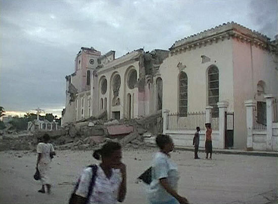 Pessoas passam pelas runas de um dos prdios destrudos pelo terremoto de 7 graus que devastou Haiti 