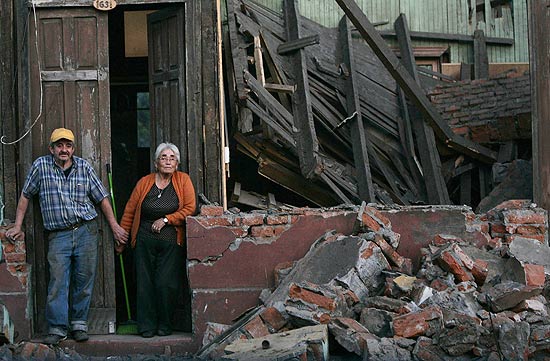 Casal chileno em frente a casa destruda por terremoto; aps tremor, cidades viram alvos de saques