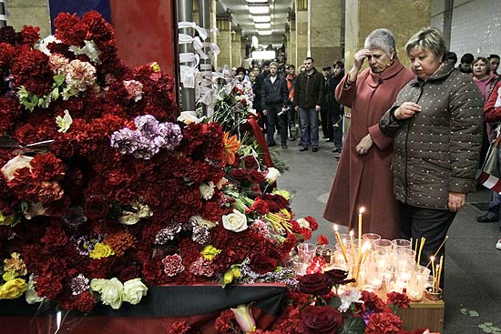 Mulheres rezam diante de velas e flores depositadas em homenagem às vítimas de duplo ataque