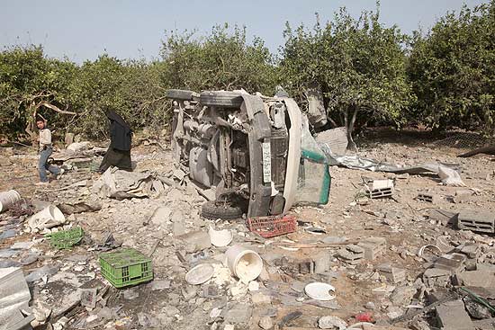Palestinos andam pelo local que antes era uma fábrica de queijos, destruída por ataques aéreos israelenses