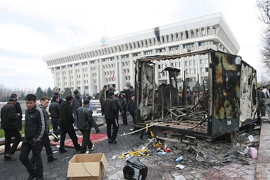 Pessoas passam pelos destroços de um caminhão incendiado durante protestos em Bishkek; novos disparos