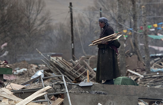 Mulher recolhe madeira em meio aos destroços do que eram casas na localidade de Jiegu, na China 