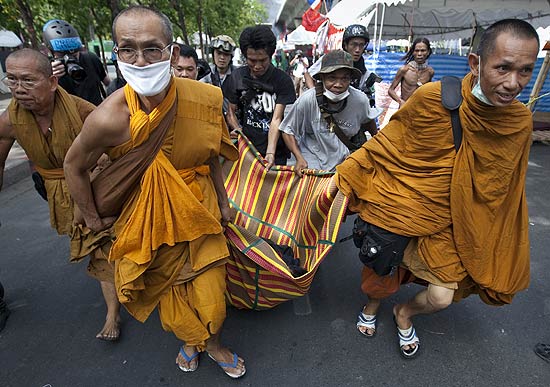 Monges budistas que apoiam os camisas vermelhas carregam corpo de homem morto por soldados