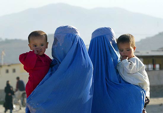 Mulheres afegãs aguardam, com seus filhos no colo, transporte em ponto de ônibus de Cabul