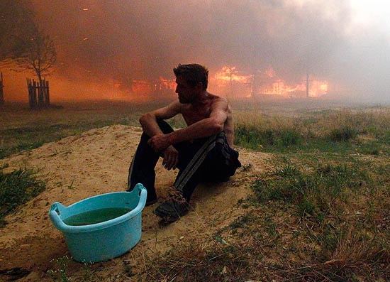 Homem senta no chão enquanto chamas consomem casa em Vyksa, na Rússia, na onda de calor extremo em 2010 