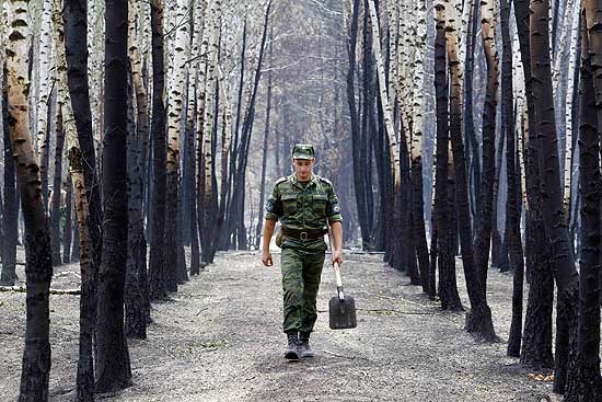 Soldado caminha por floresta consumida por incêndio florestal; clima quente e seco alimenta chamas 