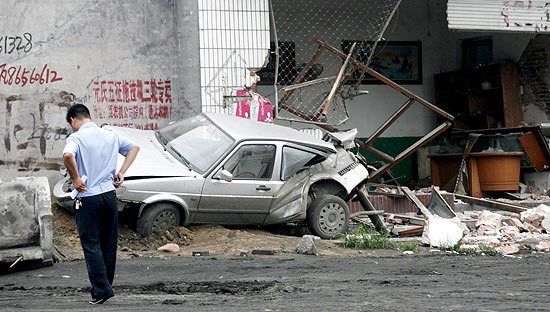 Chinês observa local onde operador de escavadeira bêbado destruiu vários veículos e prédios