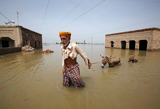 Ali Mardan leva seus dois burros pelas enchentes na vila de Karampur, no Paquisto; 1.600 morreram