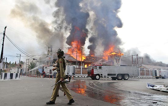 Policial patrulha as ruas de srinagar com prdio do governo em chamas ao fundo, violncia voltou  cidade 