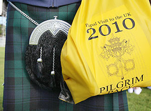 Homem usando tradicional saia escocesa carrega a mochila amarela, parte do kit que os fieis receberam