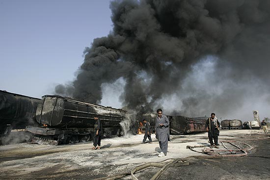 Policiais paquistaneses observam os caminhes de suprimentos incendiados por militantes