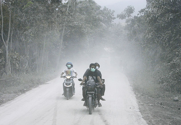 Indonésios usando máscara de proteção passam de moto por via coberto por cinzas vulcânicas após erupção do Monte Merapi