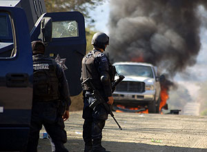 Policial olha carro queimando durante confronto com membros do cartel La Familia, em Apatzingan, no Mxico
