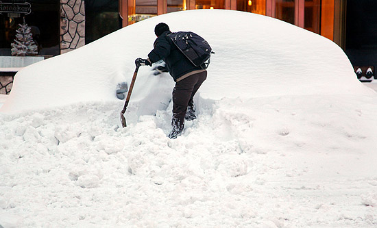 Novas iorquino tenta remover neve que cobre seu veculo em rua de Manhattan; mau tempo prejudica transportes