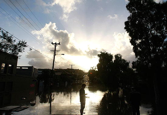 Homem  visto em rua inundada de Brisbane; cerca de 20 mil casas correm risco de serem inundadas