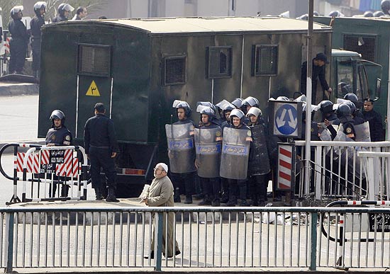 Egípcio passa por cordão de policiais antidistúrbios em uma ponte de Cairo; relatos de confrontos violentos