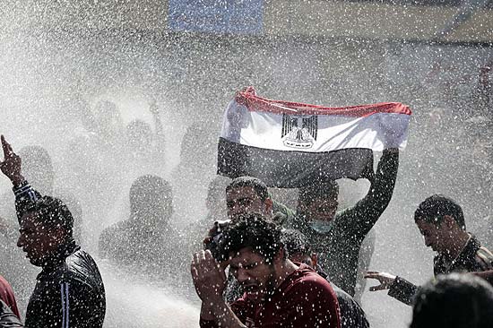 Manifestante egípcio ergue bandeira em meio à água lançada pela polícia para dispersar manifestantes