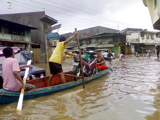 Filipinos atravessam cidade alagada em barco de madeira; ao menos 89 morreram desde o Natal 