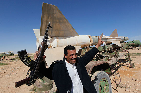 Civil líbio segura arma em comemoração diante de um míssil em base aérea abandonada em Tobruk