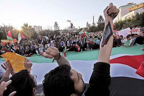 Jovens renem-se ao redor de uma grande bandeira palestina durante marcha pela unidade nacional em Gaza