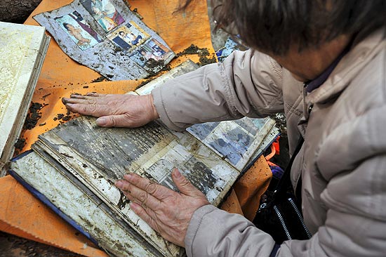 A japonesa Kuniko Komuro, de 69 anos, limpa álbum de fotos da neta, na região de Okawa, após o terremoto