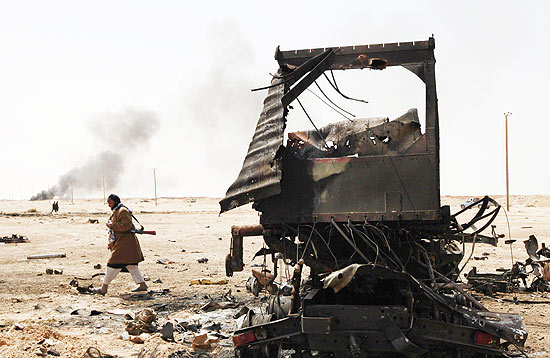 Homem caminha perto de carro queimado na cidade de Ajdabiyah, no leste da Líbia; rebeldes retomaram controle