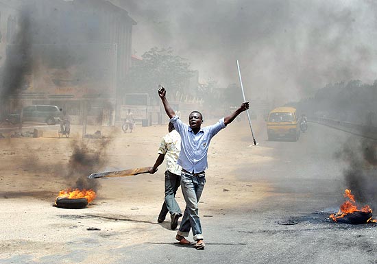 Jovens seguram paus e pedaos de metal durante protestos na cidade nigeriana de Kano