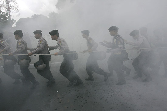 Policiais correm para evitar fumaa de pneus queimados em protesto de 1 de Maio na Indonsia