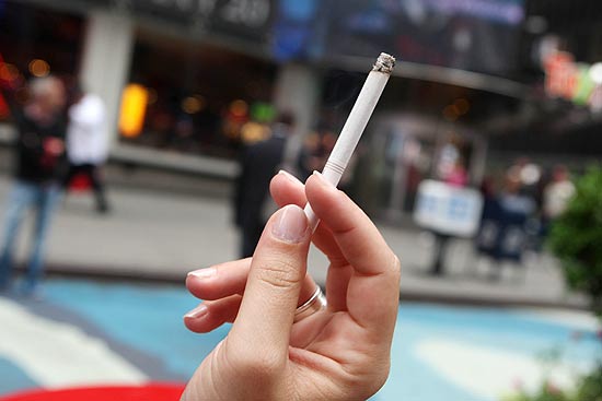 Mulher segura cigarro em calçada próxima da Times Square; NY tem queda histórica em número de fumantes